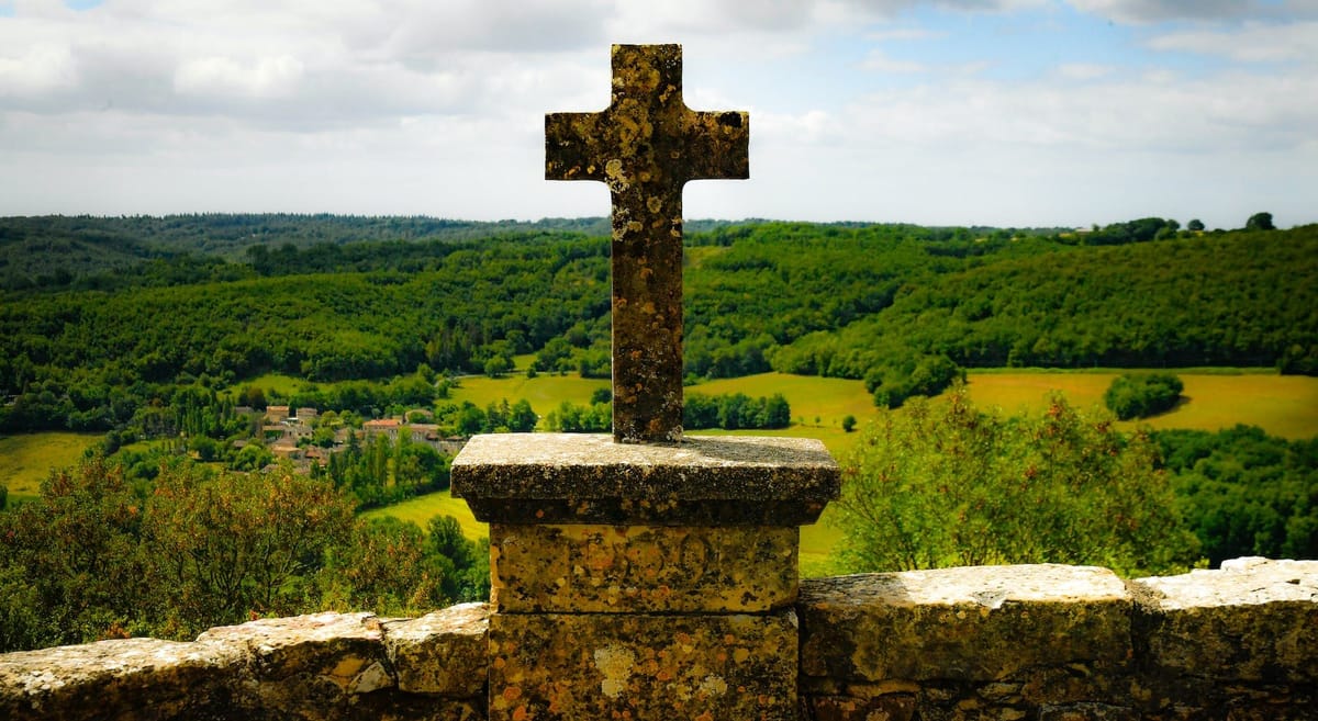 cross on stone wall over forest in countryside